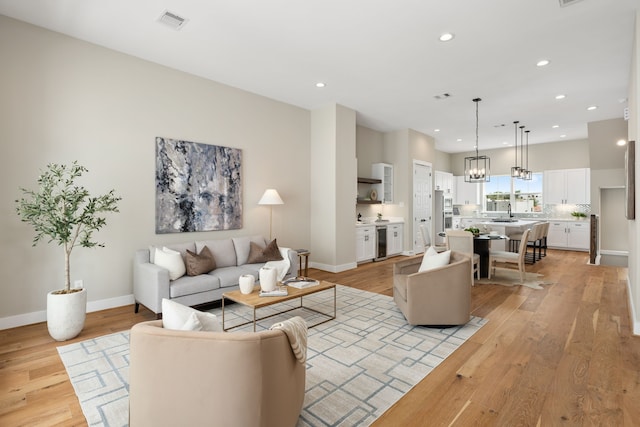 living room with a chandelier, light wood-type flooring, and beverage cooler