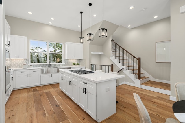 kitchen featuring decorative light fixtures, a center island, light wood-type flooring, and white cabinetry