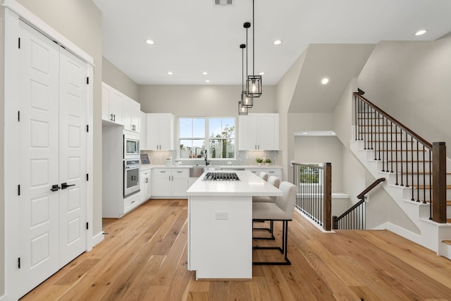 kitchen with white cabinets, light wood-type flooring, stainless steel appliances, and a kitchen island