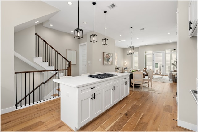 kitchen featuring stainless steel gas cooktop, decorative light fixtures, light hardwood / wood-style flooring, white cabinets, and a kitchen island