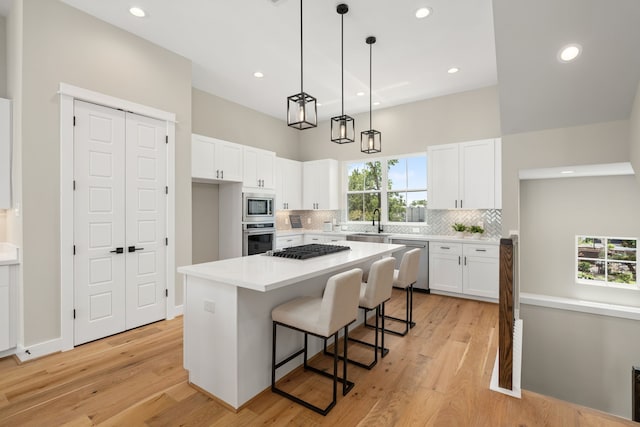 kitchen with a center island, light hardwood / wood-style floors, decorative light fixtures, white cabinets, and appliances with stainless steel finishes