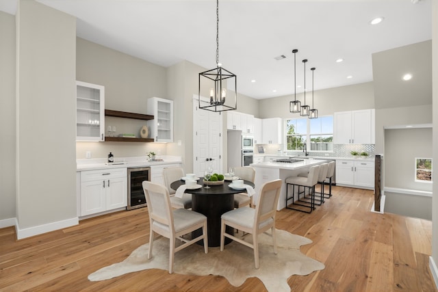 dining area featuring an inviting chandelier, light hardwood / wood-style flooring, wine cooler, and sink