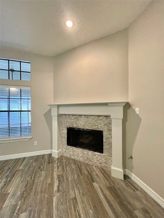 unfurnished living room featuring a textured ceiling, hardwood / wood-style flooring, and a stone fireplace