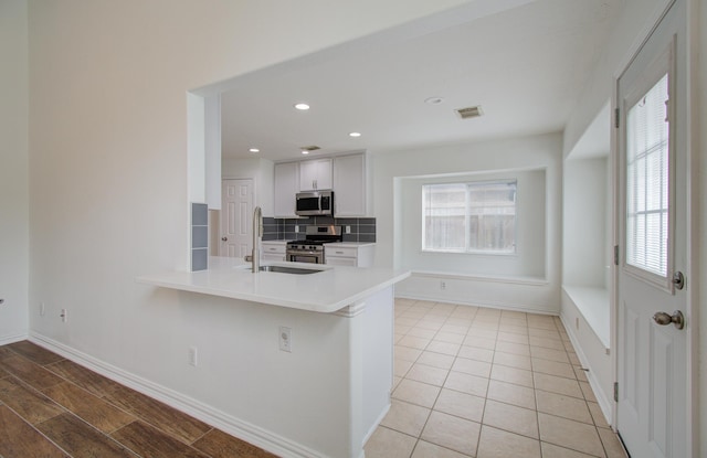 kitchen with backsplash, white cabinets, sink, appliances with stainless steel finishes, and kitchen peninsula