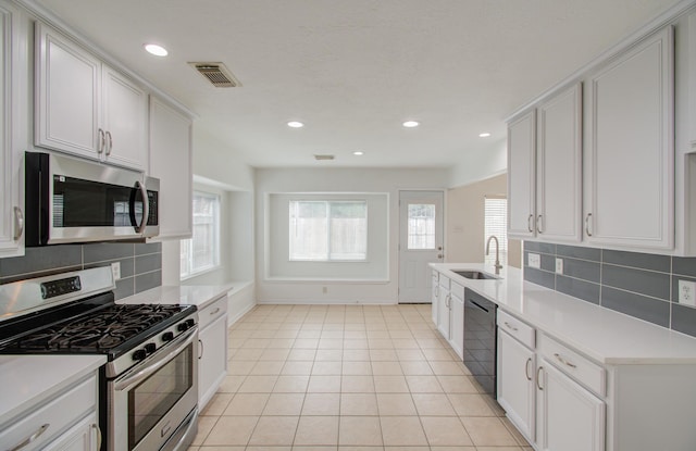 kitchen with decorative backsplash, stainless steel appliances, sink, light tile patterned floors, and white cabinetry