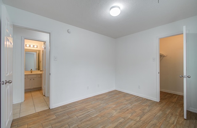 bedroom with a closet, a walk in closet, a textured ceiling, and light hardwood / wood-style flooring