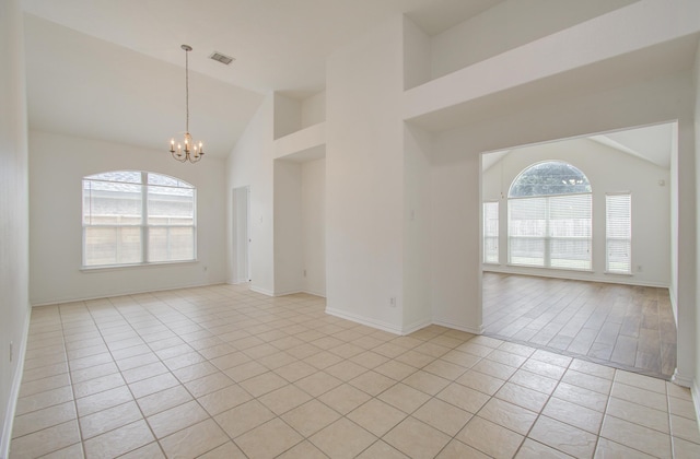 tiled empty room featuring plenty of natural light, high vaulted ceiling, and a chandelier