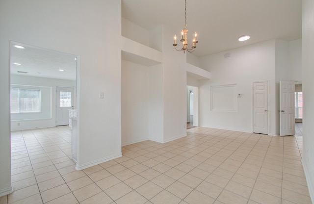 unfurnished room with light tile patterned flooring, a towering ceiling, and a chandelier