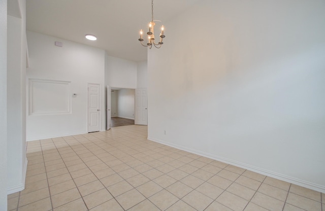 empty room with a notable chandelier, light tile patterned floors, and a high ceiling