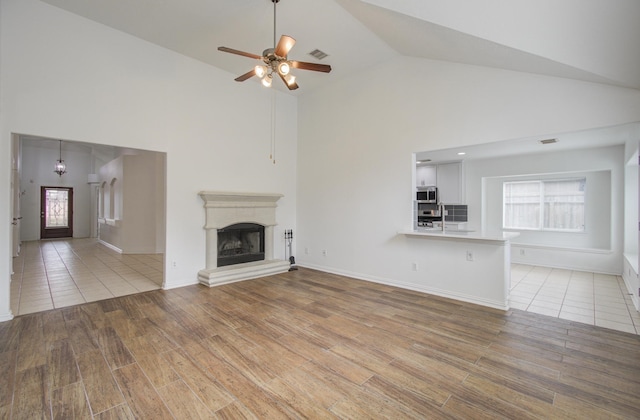 unfurnished living room featuring light wood-type flooring, high vaulted ceiling, ceiling fan, and a healthy amount of sunlight