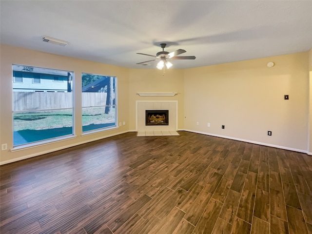 unfurnished living room featuring ceiling fan, dark wood-type flooring, and a tiled fireplace