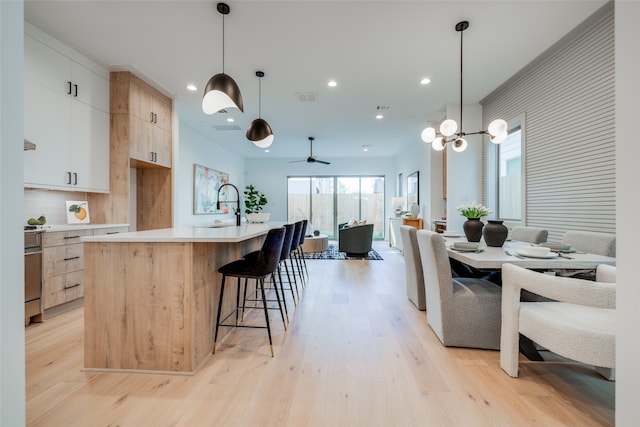 kitchen with white cabinets, decorative light fixtures, light wood-type flooring, and an island with sink