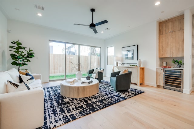 living room featuring bar area, wine cooler, light hardwood / wood-style flooring, ceiling fan, and ornamental molding