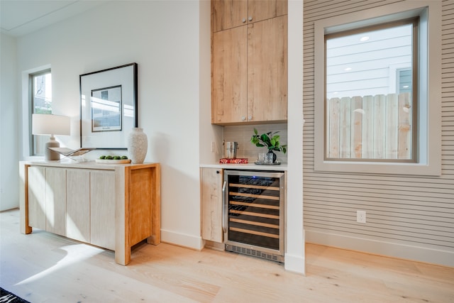 bar with backsplash, baseboards, beverage cooler, light wood-type flooring, and a bar