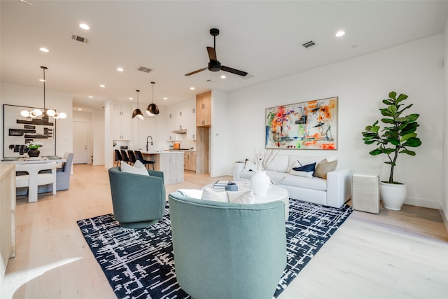 living room featuring ceiling fan with notable chandelier, light hardwood / wood-style flooring, and sink