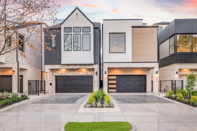 modern home with brick siding, an attached garage, fence, stucco siding, and driveway