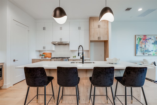 kitchen featuring white cabinetry, a center island with sink, pendant lighting, and light wood-type flooring