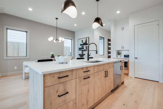 kitchen featuring light wood-style flooring, a center island with sink, light brown cabinetry, a sink, and stainless steel dishwasher