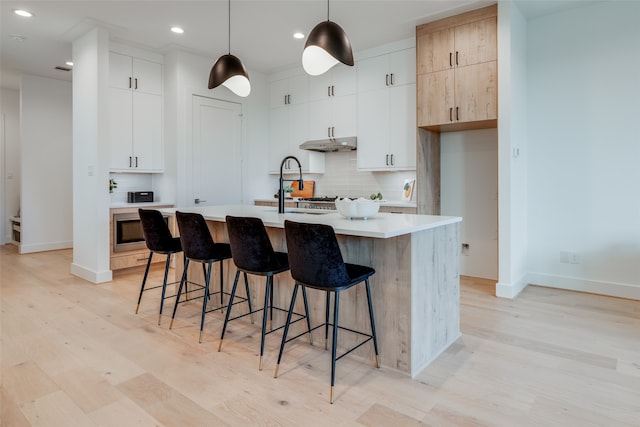 kitchen featuring tasteful backsplash, pendant lighting, a kitchen island with sink, white cabinets, and light wood-type flooring