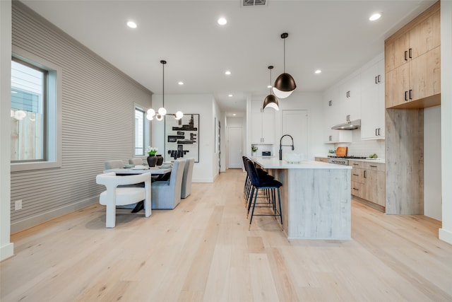 kitchen featuring light brown cabinetry, sink, light hardwood / wood-style floors, hanging light fixtures, and an island with sink