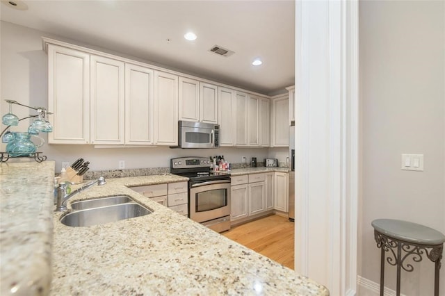 kitchen with sink, light stone counters, light wood-type flooring, stainless steel appliances, and white cabinets