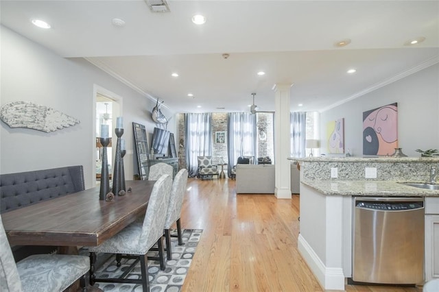 dining space with crown molding, sink, decorative columns, and light wood-type flooring