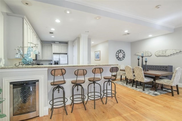 kitchen with white cabinets, stainless steel fridge, kitchen peninsula, crown molding, and light wood-type flooring