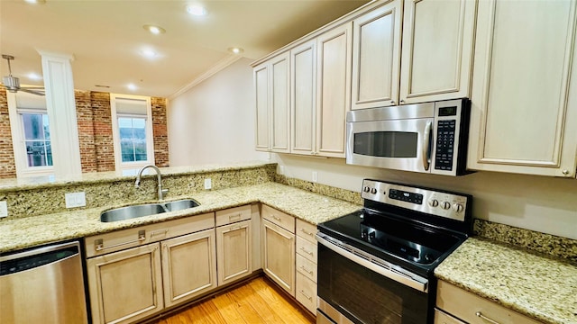 kitchen featuring appliances with stainless steel finishes, sink, light stone counters, kitchen peninsula, and crown molding