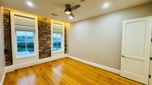 unfurnished room featuring ceiling fan, brick wall, and light hardwood / wood-style floors