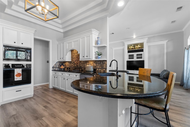 kitchen featuring light hardwood / wood-style floors, decorative light fixtures, a breakfast bar, white cabinets, and black appliances