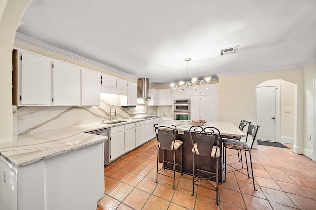 kitchen with tasteful backsplash, wall chimney exhaust hood, pendant lighting, white cabinets, and a kitchen island