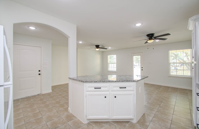 kitchen with white fridge, white cabinetry, ceiling fan, and light stone counters