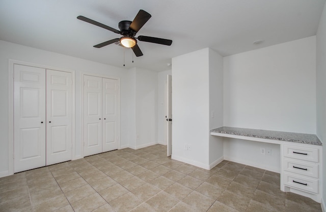 unfurnished office with built in desk, ceiling fan, and light tile patterned flooring