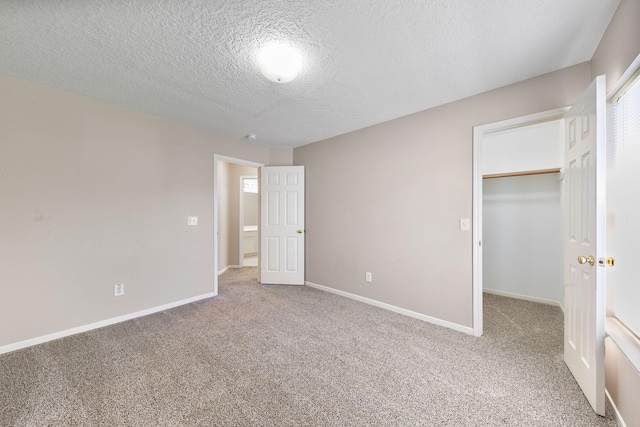 unfurnished bedroom with a walk in closet, a closet, carpet, and a textured ceiling