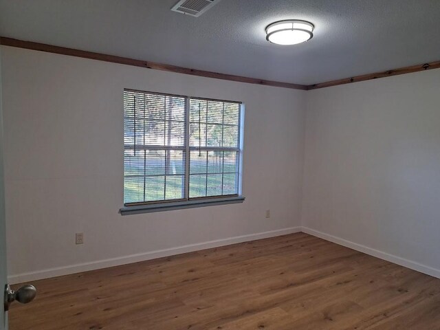 unfurnished room with hardwood / wood-style flooring, ornamental molding, and a textured ceiling