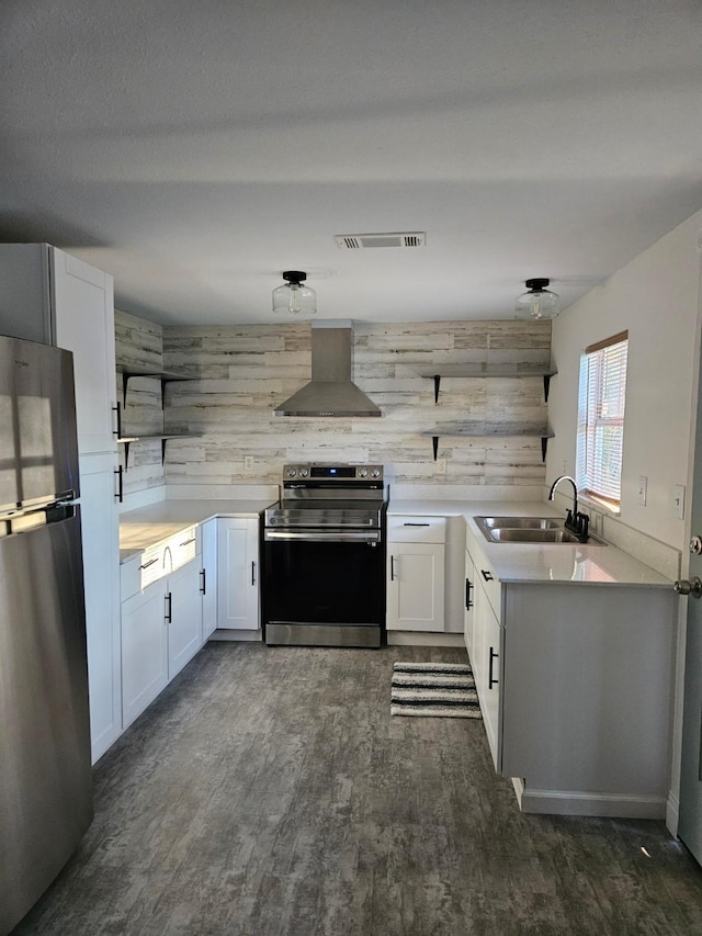 kitchen featuring appliances with stainless steel finishes, wooden walls, sink, wall chimney range hood, and white cabinetry