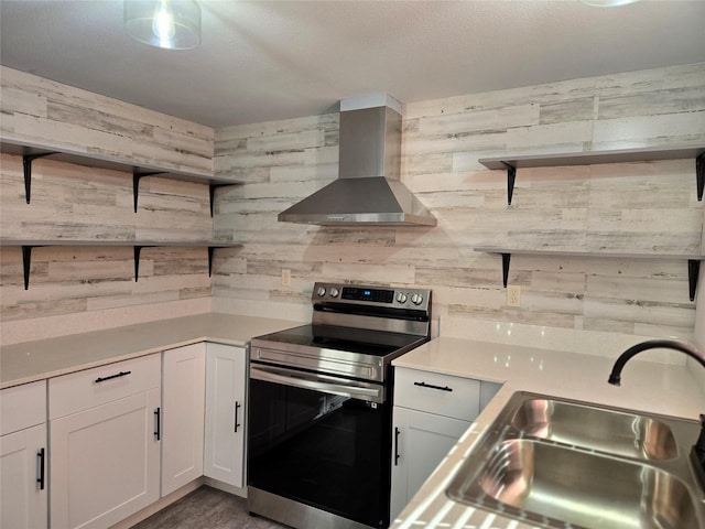 kitchen featuring stainless steel electric stove, white cabinetry, wall chimney range hood, and sink