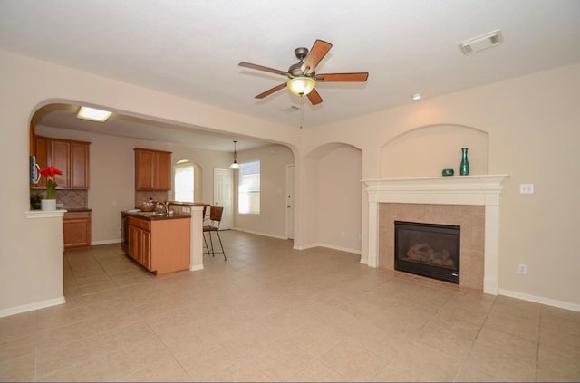 unfurnished living room with a tile fireplace, ceiling fan, sink, and light tile patterned flooring