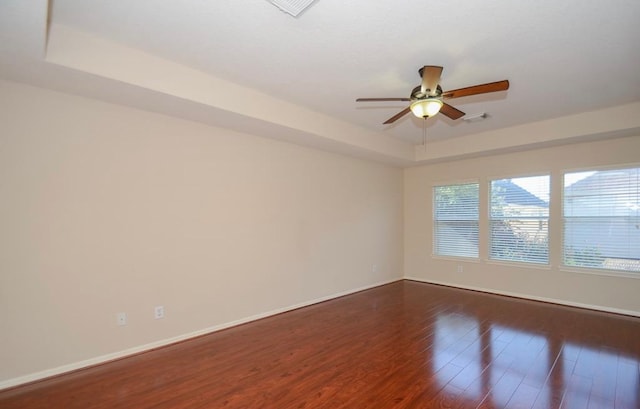 empty room featuring ceiling fan, dark hardwood / wood-style flooring, and a tray ceiling