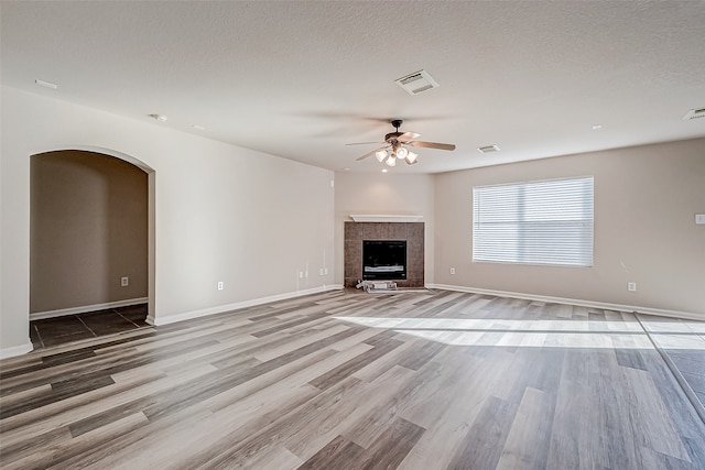 unfurnished living room with a tile fireplace, ceiling fan, a textured ceiling, and light wood-type flooring