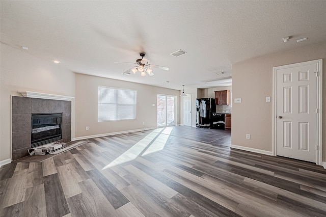 unfurnished living room featuring a fireplace, a textured ceiling, ceiling fan, and dark wood-type flooring