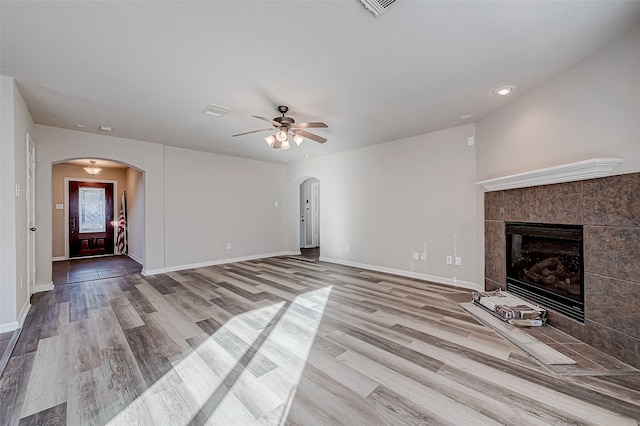 unfurnished living room featuring a tile fireplace, ceiling fan, and light wood-type flooring