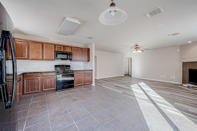 kitchen featuring black appliances, ceiling fan, decorative backsplash, a fireplace, and decorative light fixtures