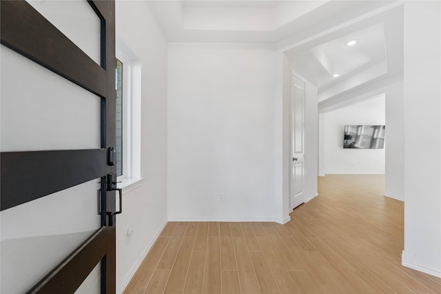 hallway with a raised ceiling and light hardwood / wood-style flooring