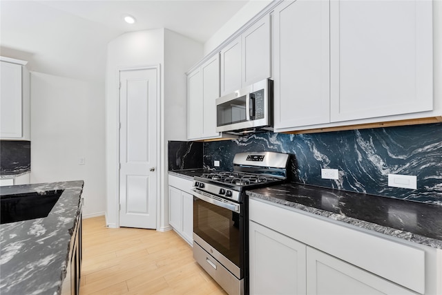 kitchen featuring decorative backsplash, dark stone counters, stainless steel appliances, light hardwood / wood-style flooring, and white cabinets