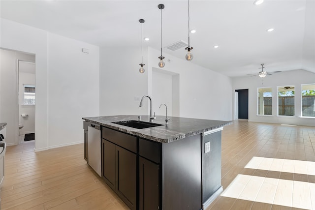 kitchen with ceiling fan, sink, stainless steel dishwasher, dark stone counters, and a kitchen island with sink