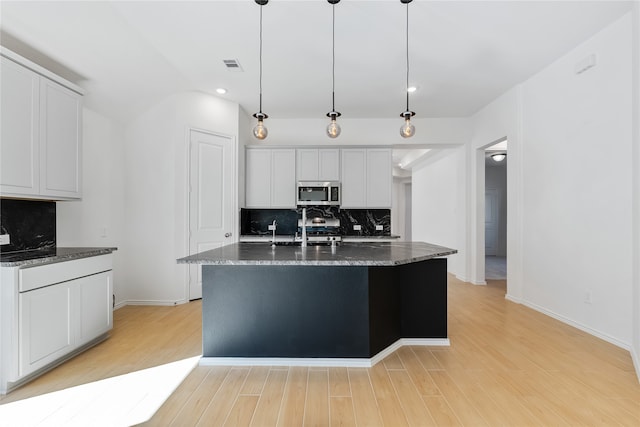 kitchen with hanging light fixtures, decorative backsplash, a kitchen island with sink, white cabinets, and appliances with stainless steel finishes