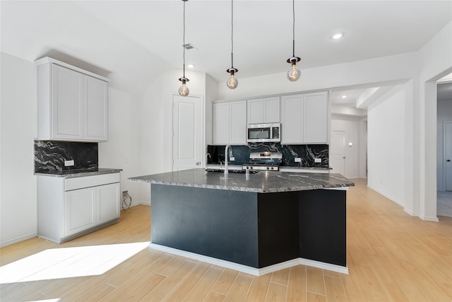 kitchen with a kitchen island with sink, light wood-type flooring, backsplash, and appliances with stainless steel finishes