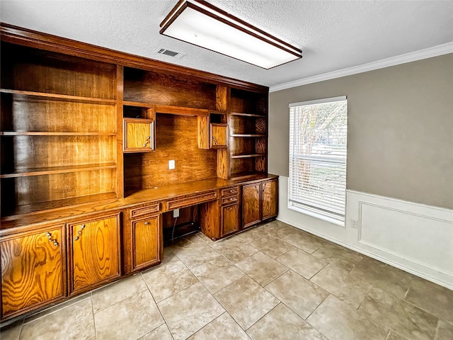 unfurnished office with a textured ceiling, built in desk, ornamental molding, and light tile patterned floors