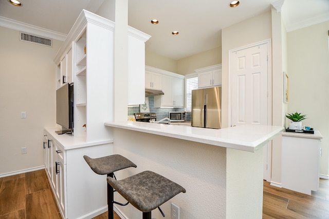 kitchen with kitchen peninsula, appliances with stainless steel finishes, a kitchen breakfast bar, hardwood / wood-style floors, and white cabinetry